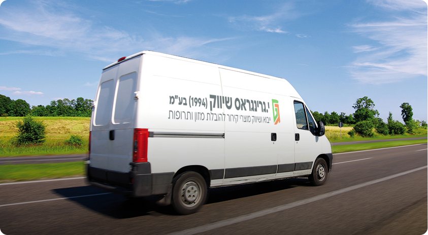 טנדר משלוחים לבן, שעל צדו כתובית בעברית, ואשר ככל הנראה מוביל מוצרים איכותיים בשרשרת הקירור, נוסע בכביש המוקף בשדות ירוקים ועצים, תחת שמיים כחולים ועננים דקים.